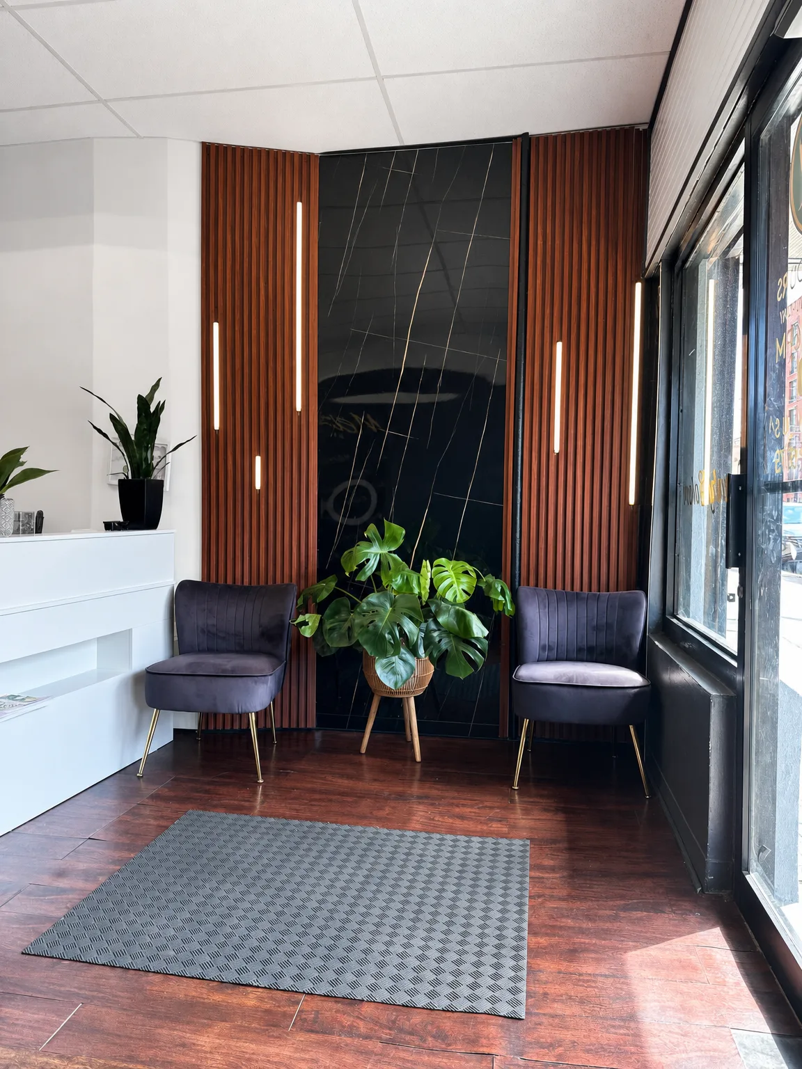 Waiting lounge at Melany's — velvet chairs, black marble and warm wood slat wall